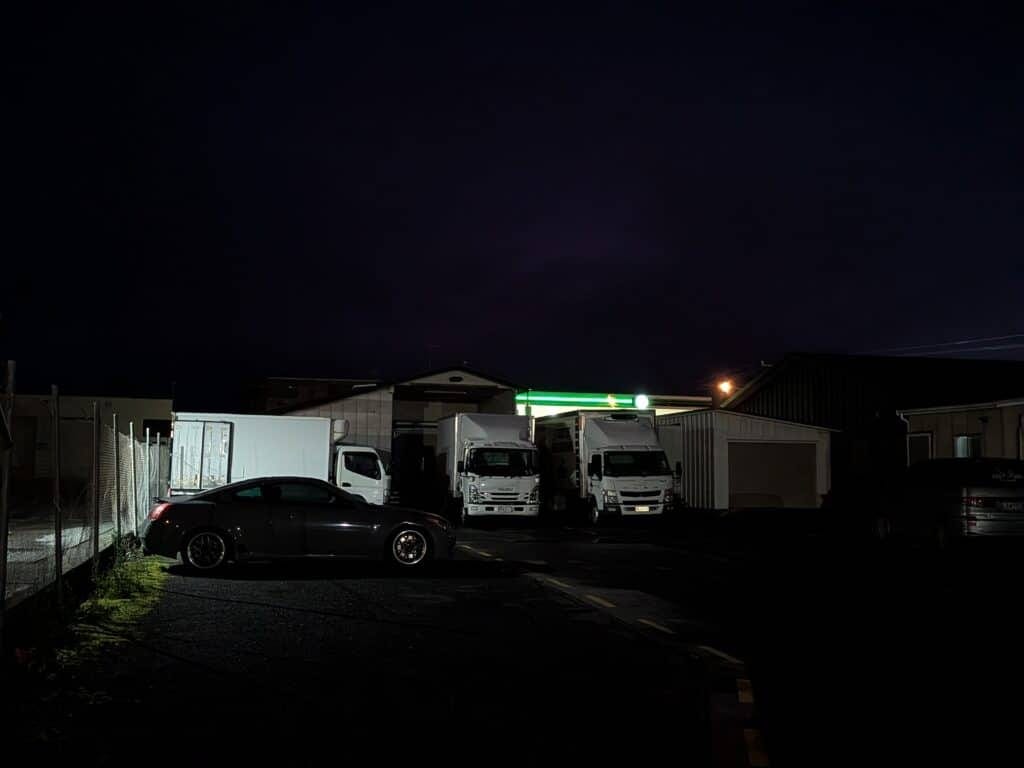 Nighttime parking lot with white delivery trucks and minimal surrounding buildings.