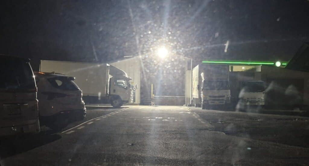 Nighttime loading dock with parked trucks, bright central light, and rain on the lens creating bokeh.