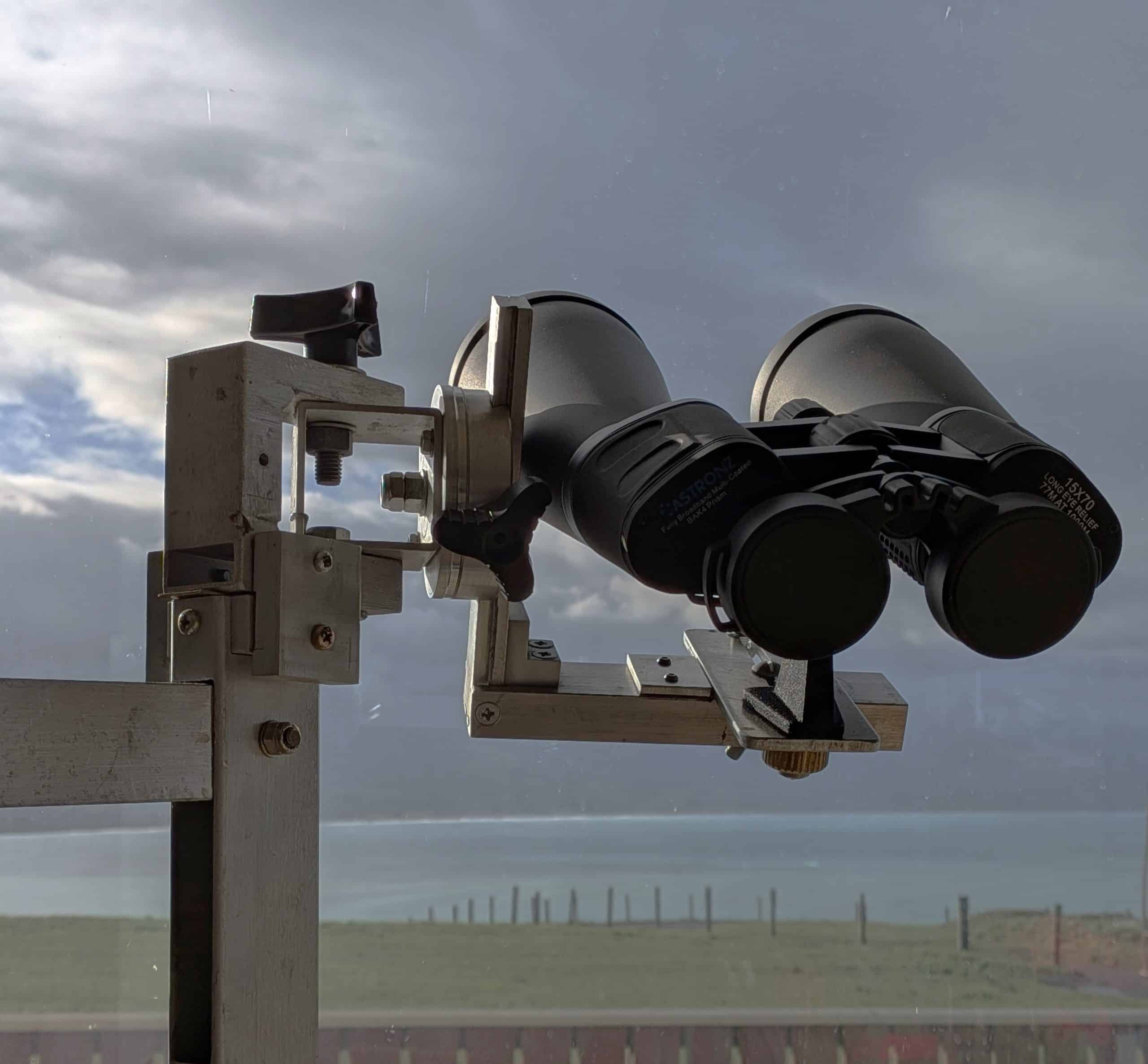 Close-up of a telescope eyepiece mounted on a wooden frame outdoors under a cloudy sky.