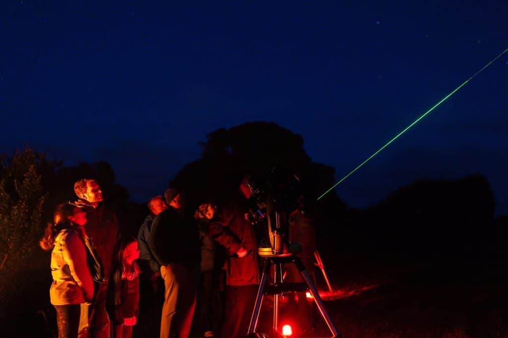 Group of people observing a green laser beam from a telescope at night.