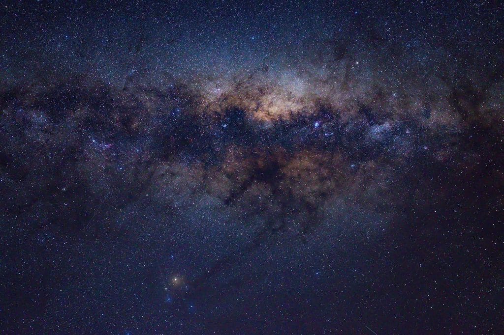 Wide view of the Milky Way across a star-filled night sky with dust lanes and nebulae.