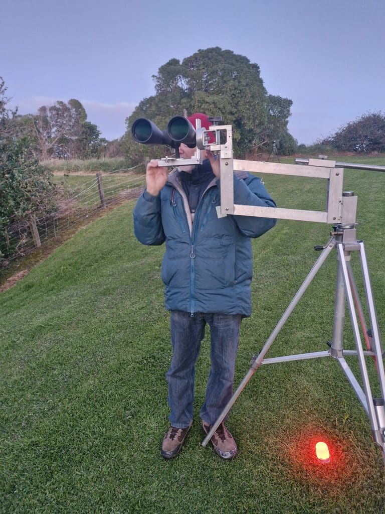 Person in teal jacket uses dual-binocular telescope on metal frame outdoors